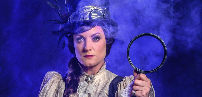 Eine Frau in historischer Kleidung hält eine Lupe in der Hand. Der Hintergrund ist mystisch mit blauem Rauch. | © SLT / Tobias Witzgall