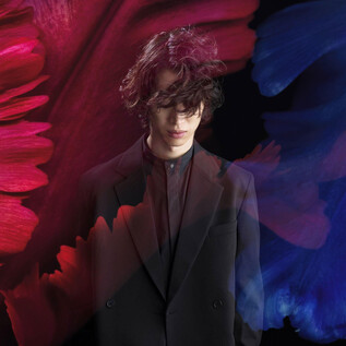 A young man stands in a black suit against a colored background. Red and blue brush strokes surround him, giving the picture an artistic touch. | © RyuyaAmao