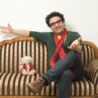 Muž sedí s úsměvem na gauči a má roztažené ruce. Vedle něj je malý, chlupatý pes. | © Wolfgang Lienbacher