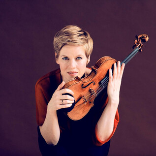 A woman holds a violin and looks directly at the camera. The background is in soft shades of brown. | © Felix Broede