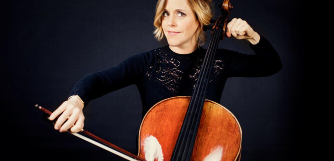 A woman plays cello against a dark background. She looks focused and holds the bow in her hand. | © Julia Wesely