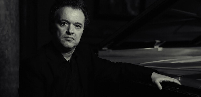 A man is sitting at the piano and looking seriously at the camera. The monochrome shot conveys an elegant and contemplative atmosphere. | © Philip Andrukovich