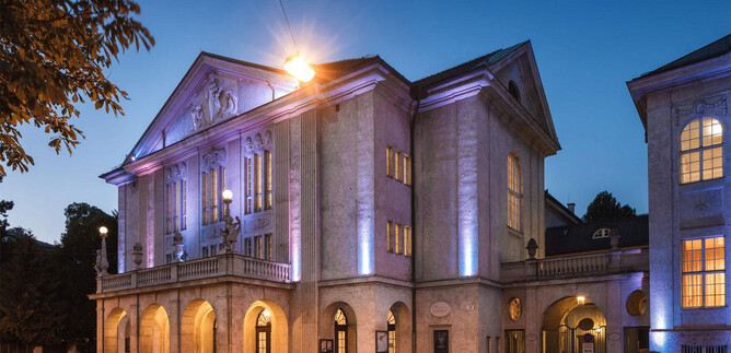 A historic building with impressive architecture, illuminated in soft colors. It is located in an urban setting at dusk. | © Christian Schneider