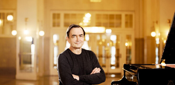 A musician sits smiling in front of a piano. In the background are elegant rooms with warm light. | © Julia Wesely