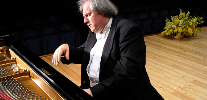 A pianist plays intensely at the piano. In the background, fresh flower arrangements can be seen. | © Vico Chamla