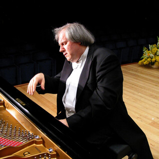 A pianist plays intensely at the piano. In the background, fresh flower arrangements can be seen. | © Vico Chamla