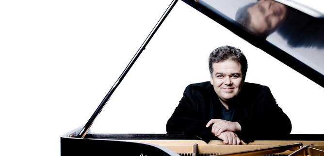 A musician smiles beside an open piano. The background is bright and simple, which draws the focus on him and the piano. | © Marco Borggreve