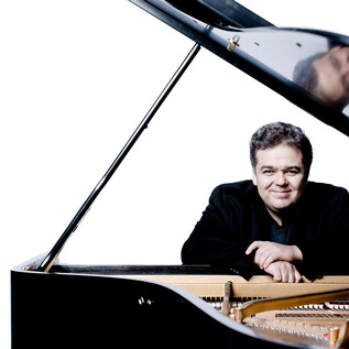 A musician smiles beside an open piano. The background is bright and simple, which draws the focus on him and the piano. | © Marco Borggreve