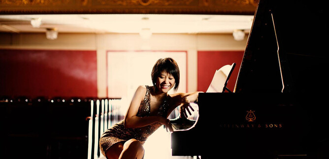 A smiling pianist sits at a piano in an elegant hall. The room is brightly lit and conveys a festive atmosphere. | © Julia Wesely