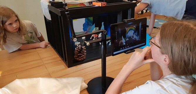 Children experiment with a creative film set environment. An adult observes them as they work with props and a camera. | © DomQuartier