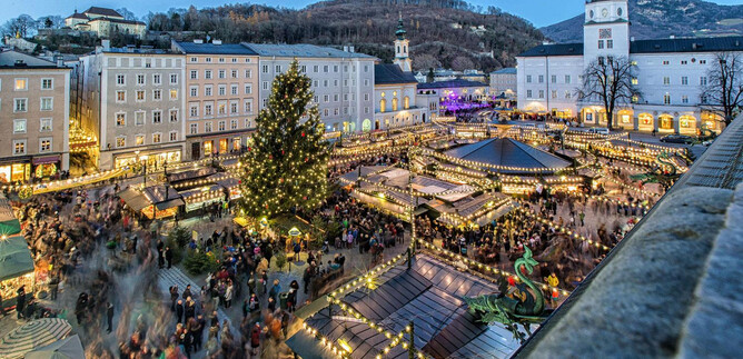 A festive Christmas market with many lights and stalls. In the middle stands a large, decorated Christmas tree. | © christkindlmarkt.co.at_Neumayr