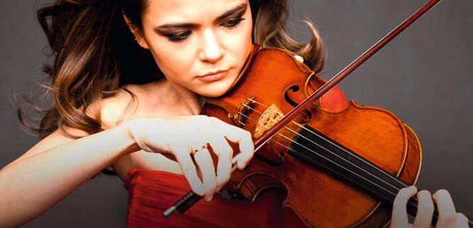 A talented violinist passionately plays her instrument. She is wearing a red dress and has long, flowing hair. | © o.A.