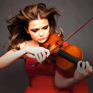 Une violoniste talentueuse joue passionnément de son instrument. Elle porte une robe rouge et a de longs cheveux fluides. | © o.A.