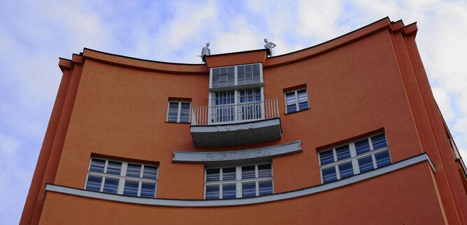 A modern orange building with a curved design. It has several windows and a balcony in the middle. | © Mag. Christoph Koca