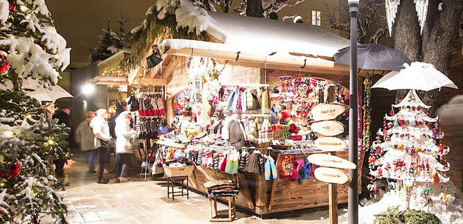 Ein festlicher Weihnachtsmarkt mit einem Holzstand, der farbenfrohe Handwerksartikel anbietet. Die Umgebung ist von Schnee bedeckt und mit dekorativen Lichtern geschmückt. | © Sternadvent Salzburg