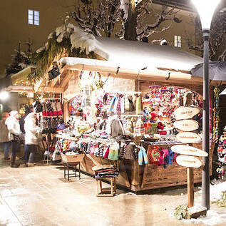 Un marché de Noël festif avec un stand en bois qui propose des articles artisanaux colorés. L'environnement est recouvert de neige et décoré de lumières. | © Sternadvent Salzburg