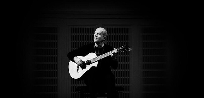 Ein Musiker sitzt auf einem Stuhl und spielt Gitarre. Die Szene ist in Schwarz-Weiß gehalten und strahlt eine ruhige Atmosphäre aus. | © Laura Pleiffer