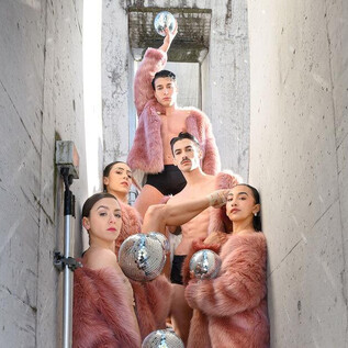 Eine Gruppe von Menschen in rosa Fellen steht in einem engen, grauen Gang. Sie halten silberne Objekte in den Händen und posieren für das Foto. | © SLT / Christian Krautzberger