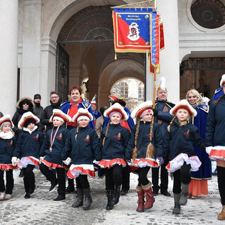 Eine Gruppe von Kindern in traditionellen Kostümen steht auf einer Straße bei einer Veranstaltung. Im Hintergrund sind Zuschauer und Dekorationen zu sehen. | © 1. Salzburger Faschingsgilde