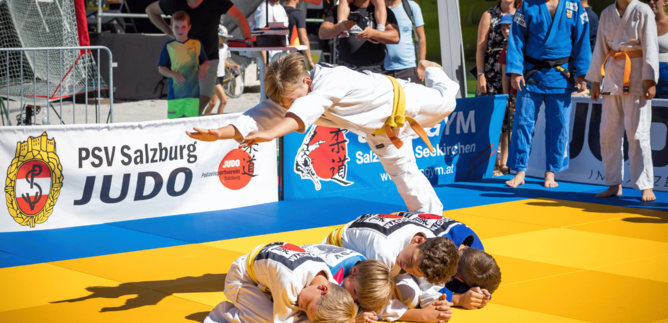 Eine Judo-Vorführung auf einer Matte mit mehreren jungen Kämpfern. Ein Athlet springt über seine Trainingspartner und zeigt eine beeindruckende Technik. | © Wild + Team Fotoagentur GmbH