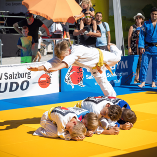 Eine Judo-Vorführung auf einer Matte mit mehreren jungen Kämpfern. Ein Athlet springt über seine Trainingspartner und zeigt eine beeindruckende Technik. | © Wild + Team Fotoagentur GmbH