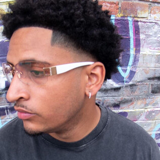 A young man with curly hair and fashionable glasses stands in front of a colorful graffiti wall. He looks thoughtfully to the side. | © Timmi Adesanya