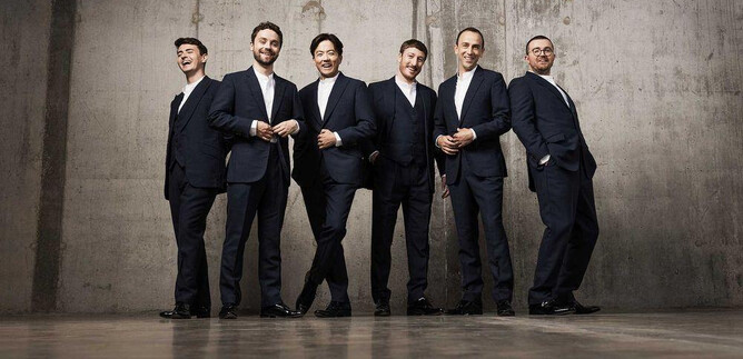 Six men in elegant suits stand next to each other in a modern room. The background is simple and has an industrial feel. | © Benjamin Ealovega