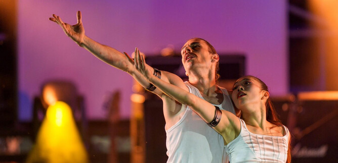 A pair of dancers performs an impressive act on a stage. They move elegantly in the spotlight. | © J. Bollwein