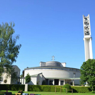 Eine große Gruppe von Menschen steht vor einem kunstvollen Brunnen. Sie tragen schwarze Kleidung mit roten Akzenten und posieren in einer winterlichen Umgebung. | © Parrkirche Herrnau