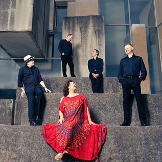 Eine Gruppe von fünf Personen posiert auf einer steinernen Treppe. Die Frau in der Mitte trägt ein auffälliges rotes Kleid, während die anderen in schwarz gekleidet sind. | © Bernhard Eder