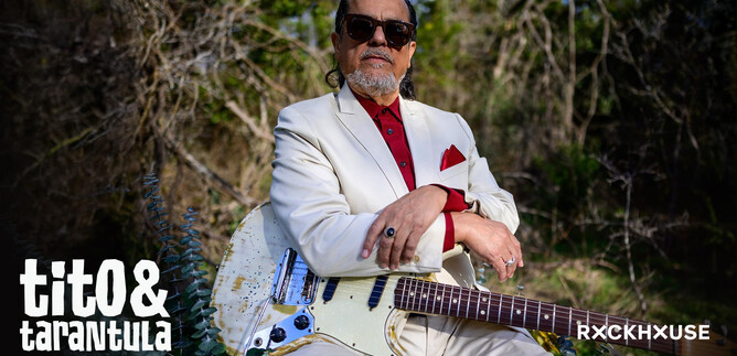 A musician is wearing an elegant white suit and sunglasses. He is sitting outdoors with an electric guitar. | © Lolita Carroll Larriva