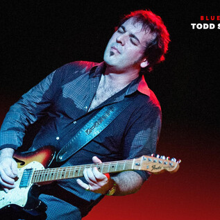 Egy zenész gitározik a színpadon. A világítás dinamikus hangulatot teremt. | © Marco van Rooijen