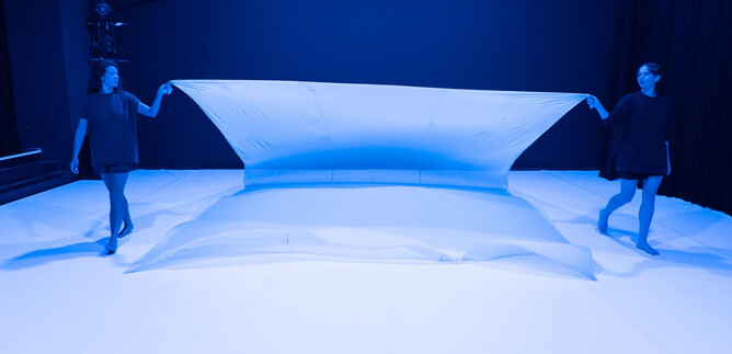 Dos mujeres tiran de una gran tela blanca en una habitación azul. La atmósfera es futurista y de un estilo minimalista. | © Fabian Schober