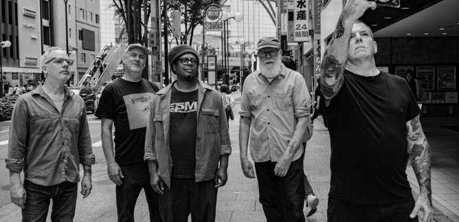 Eine Gruppe von fünf Männern steht in einer Stadtstraße. Sie schauen in verschiedene Richtungen, während einer von ihnen ein Selfie macht. | © Yusuke Nagata