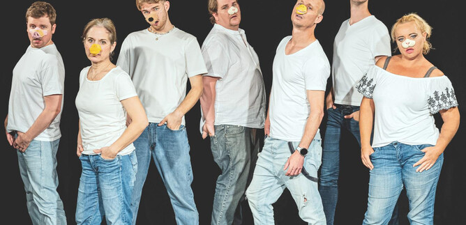 Eine Gruppe von acht Personen steht in einer Reihe, gekleidet in weiße T-Shirts und Jeans. Ihre Gesichter sind kreativ bemalt, was ihre ausdrucksvollen Posen verstärkt. | © Taro Ebihara