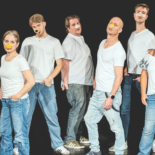 Eine Gruppe von acht Personen steht in einer Reihe, gekleidet in weiße T-Shirts und Jeans. Ihre Gesichter sind kreativ bemalt, was ihre ausdrucksvollen Posen verstärkt. | © Taro Ebihara