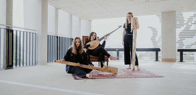 Tres músicas están sentadas en un espacio moderno y tocan diferentes instrumentos musicales. Llevan ropa negra y parecen creativas y relajadas. | © Anna Haslauer
