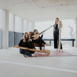 Trois musiciennes sont assises dans une pièce moderne et jouent de différents instruments de musique. Elles portent des vêtements noirs et semblent créatives et détendues. | © Anna Haslauer