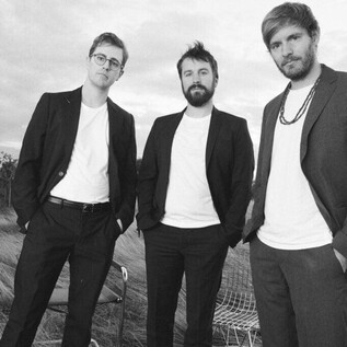 Trois hommes en costumes se tiennent dans un champ ouvert. Ils ont l'air confiants et sont photographiés dans un style noir et blanc moderne et artistique. | © Julian Hagen