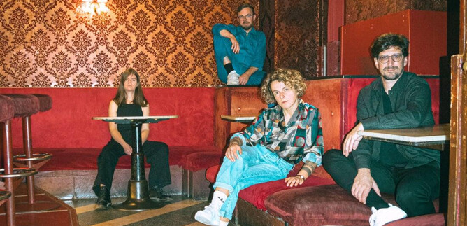 Eine Gruppe von vier Personen sitzt und steht in einem stilvollen, rot dekorierten Raum. Die Atmosphäre ist entspannt und kreativ. | © Julia Freytag