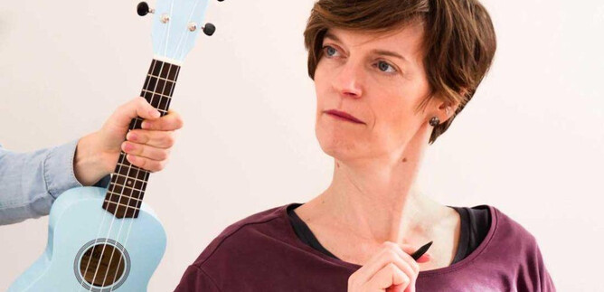 A woman looks thoughtful while someone in the background holds a light blue ukulele. She seems to have a pen in her hand and is in a creative moment. | © Klemens Dellacher