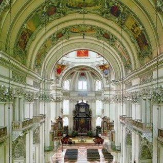 An impressive church with a high ceiling and ornate ceiling paintings. The interior view shows a symmetrical arrangement of pews and a lavish altar. | © Kunst & Kultur