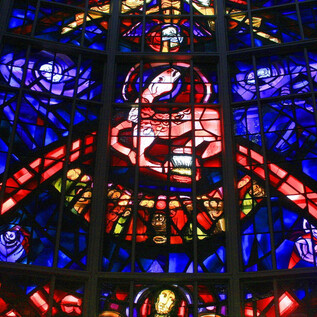 A colorful stained glass window with bright colors and intricate patterns. It features religious motifs in an artistic representation. | © Universität Mozarteum