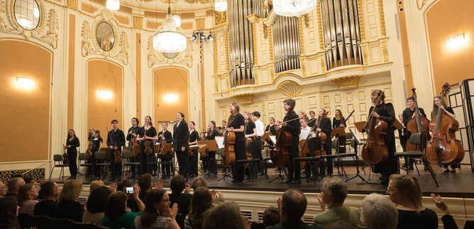 An orchestra is on stage in a magnificent hall. The audience is applauding enthusiastically. | © Wol
