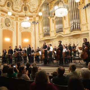 An orchestra is on stage in a magnificent hall. The audience is applauding enthusiastically. | © Wol