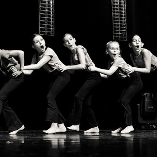 Five dancers stand in a line and display various expressions. They are wearing black clothing and dancing on a stage. | © Georg Kritsch