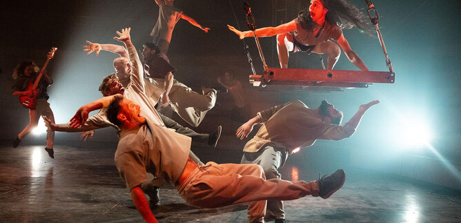 Eine beeindruckende Tanzaufführung mit mehreren Tänzern in dynamischen Posen. Eine Tänzerin schwingt an einer Schaukel, während die anderen um sie herum agieren. | © Kalimba