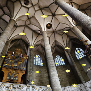 A large church space with high columns and an impressive organ. The ceiling is adorned with shining stars, creating a festive atmosphere. | © Markus Stepanek