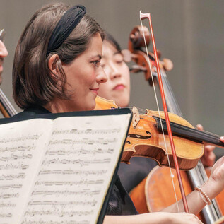 A group of musicians is playing in an orchestra. The violinist in the middle is focused on her sheet music. | © Universität Mozarteum