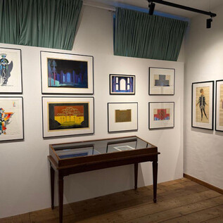 A creative gallery with various artworks on the wall. In the center stands a wooden table with a glass top. | © Wolfgang Lienbacher